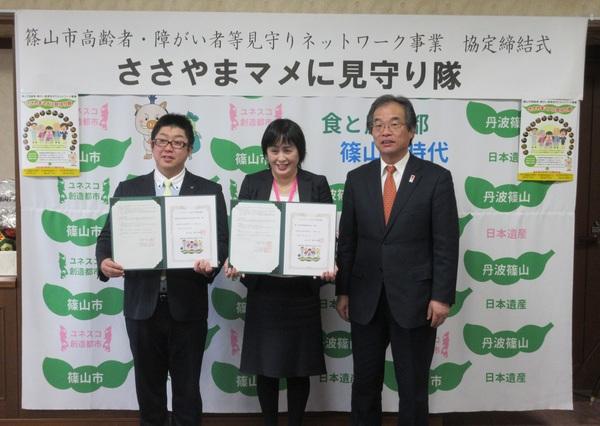 メガネをかけた男性2人とその間に女性が1名立っていて、協定書を手にもって見せている写真