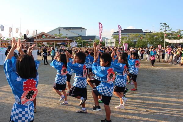 子供達が法被にうちわを背にさし、踊っている写真