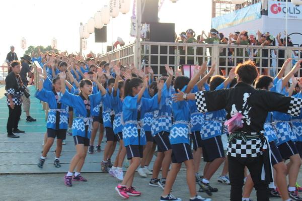 水色のハッピ姿で踊っている人達がちょうど踊りの列の曲がり角にさしかかったので黒のはっぴ姿の男性が両手をひろげ誘導している写真