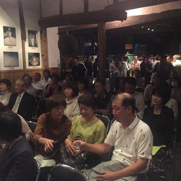 ステージを見ながら椅子に座った男性が女性にお酒を注いでもらっている写真