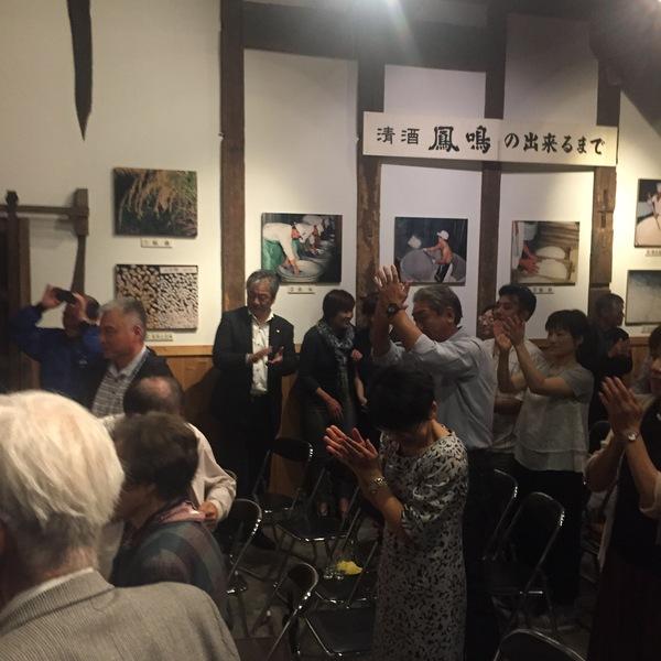 椅子から立ち上がりたくさんの人達が拍手をしている写真