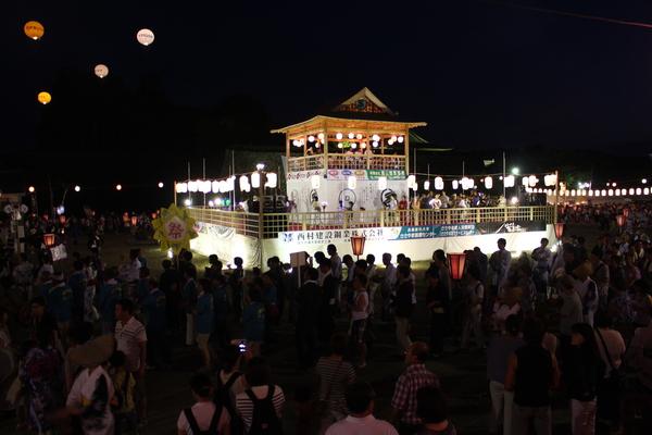 舞台がライトアップされ会場にきている人達がみんなで踊りを踊っている全体写真