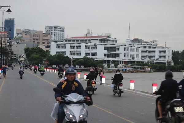 白い建物が奥にたち近くを通る道路にたくさんのバイクが走っている写真