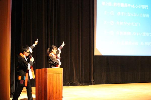 男女の司会者がスクリーンに向かって指をさしている写真