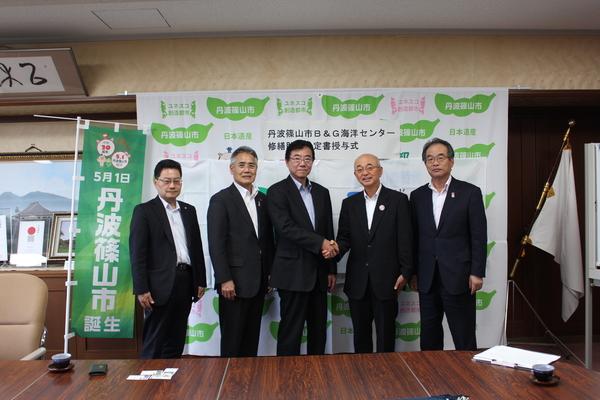 握手をしている市長と男性、その横に並ぶ男性関係者の写真