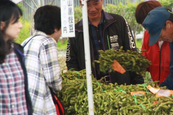 販売ブースに束になってる黒枝豆がたくさん置いてあり、それを手に取っている人や見ている人々の写真
