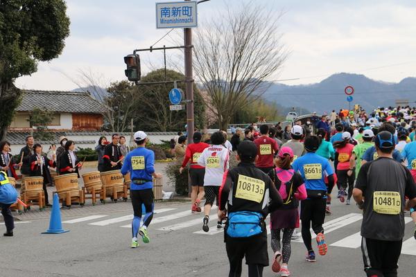 選手が一生懸命走っている中、沿道では法被を着た女性の方々が樽太鼓を叩いて応援している写真