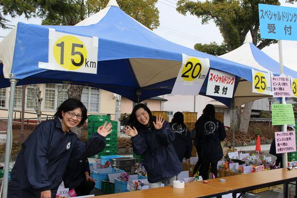 青と白の縞々のテントの中でスタッフが笑顔で手を振っている写真