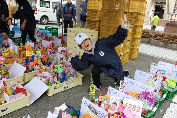 プラスチック食品用コンテナの中にカラフルなペットボトルが沢山置いてある中、中腰の体勢で笑顔でピースしている女性の写真