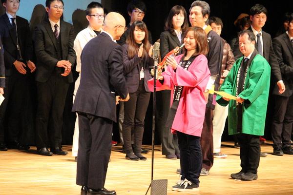 女性職員が市長からトロフィーをもらっている写真