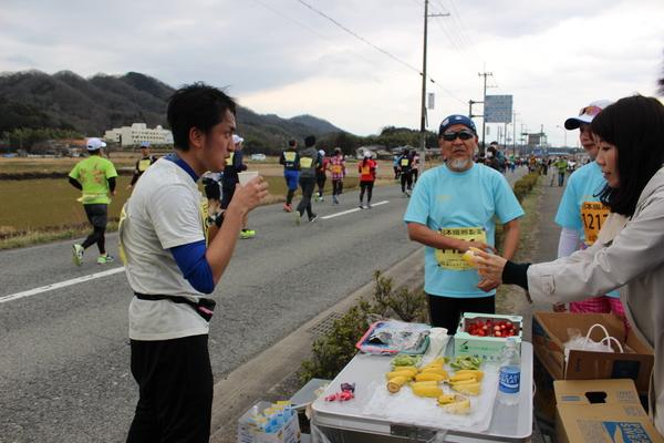選手が途中休憩をとり紙コップで飲み物を飲んでいて、スタッフと話をしている写真