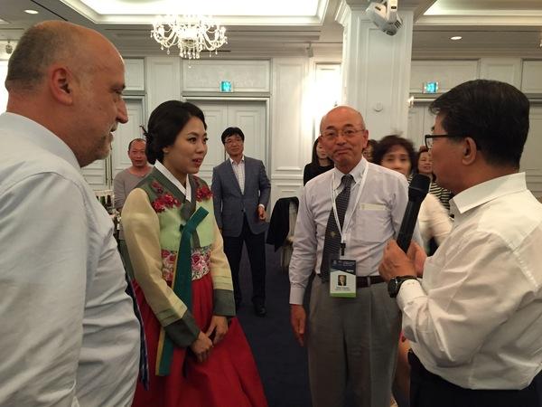 マイクを持った男性を、チマチョゴリを着た女性と市長と男性1人が、見ている写真