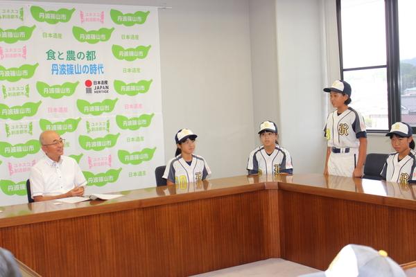 市長が笑顔で見守る中、ユニフォーム姿の女の子が立っている写真