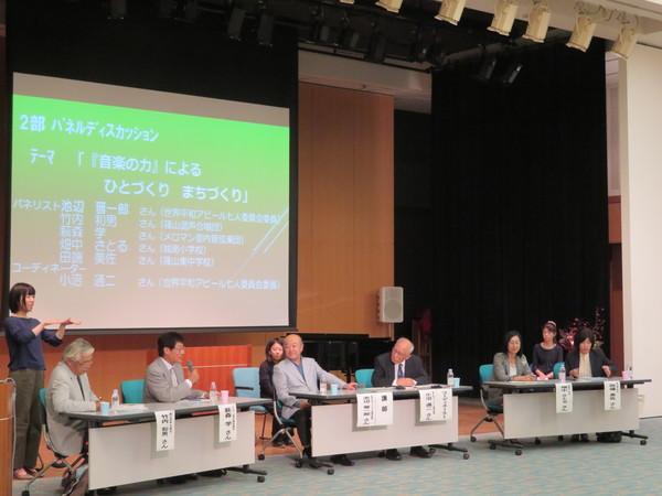 スクリーンの前に座ってディスカッションしている池辺 晋一郎さん、竹内 和男さん、萩森 学さん、畑中 さとるさん、田端 美佐さん、小沼 通二さんと手話通訳の3人の女性の写真