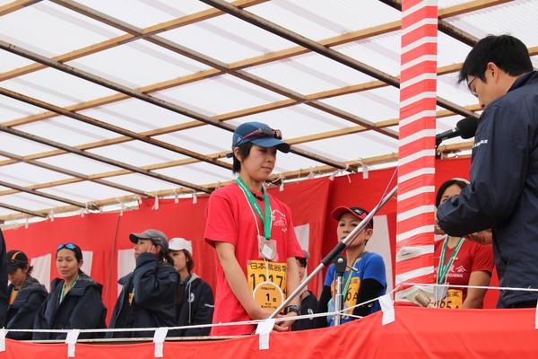マラソン大会に出場した女性が紅白幕の中で表彰されている写真