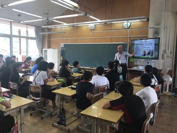 教室の中で市長がテレビ画面を指差しながら生徒たちに説明している写真