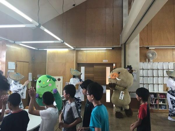 市のゆるキャラマスコット人形2体とおけさ傘を頭に被って白色の着物姿の踊り手3名に加わって子供たちが一緒に見様見真似で踊っている写真