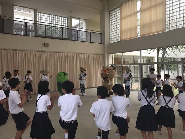 マスコットキャラクターや踊りてと生徒皆で輪になって片足を上げて踊っている写真