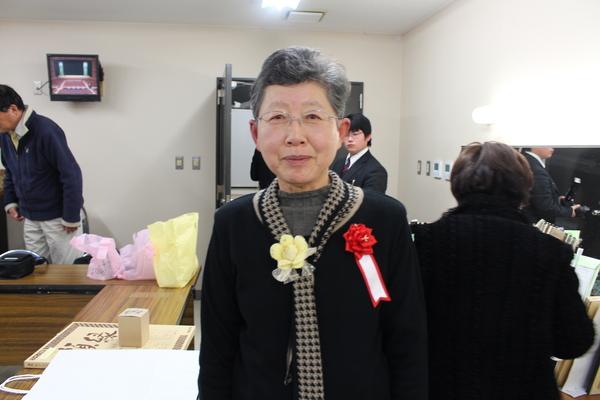 胸に赤いリボンを付けた女性が控室で記念撮影している写真