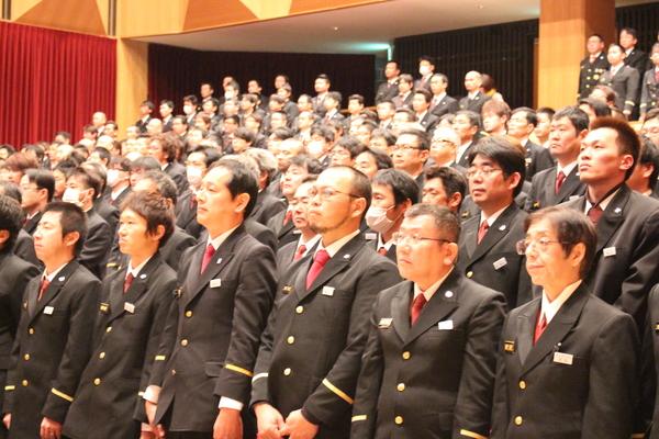 制服姿の男性らが客席で立って話を聞いている写真