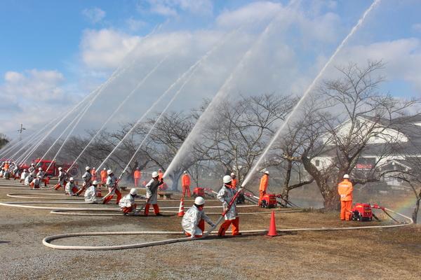 放水演習している消防団員らの後ろ姿の写真