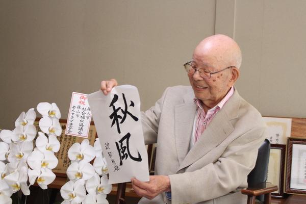 「秋風」との書いた書の半紙を持って写っている波部 時雄さんの写真