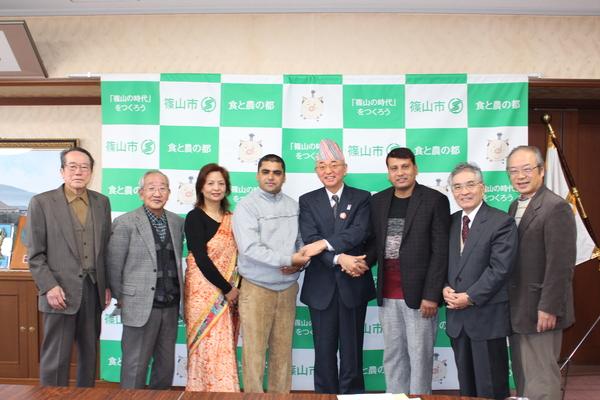 市長が手を交差し、サプコタ学校長とは右手で、ネパールさんとは左手で握手をし、篠山ナマステ会の方々と写っている集合写真