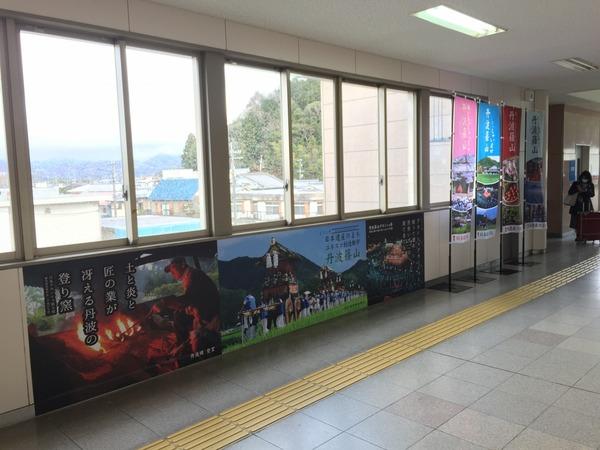 篠山口駅内の壁に篠山のポスターや旗があり、ガラスの外には篠山の町が見えている写真