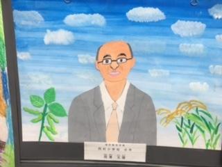 背景が青空で無数の雲が浮かんでおり、中央にグレーの背広を着た市長が描かれている似顔絵の写真