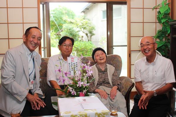 ご高齢の女性を複数の大人が囲み笑顔で正面を向いている写真