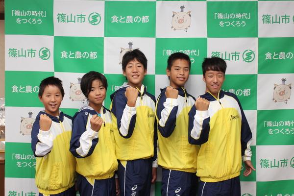 西紀スイミングスクールの生徒5名が黄色と青色の入ったジャンパーを着て右手でガッツポーズをして写っている写真