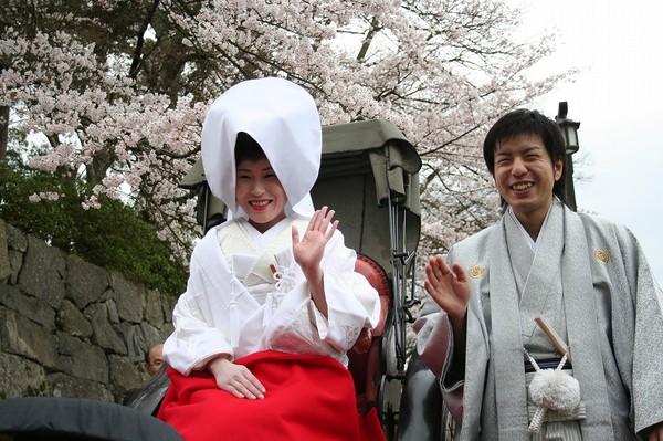 桜が満開の中、新郎と新婦が手を挙げ微笑んでいる写真