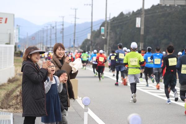 走ってくる大勢のランナーに手を叩いて応援している2名の女性と2名の子供の写真