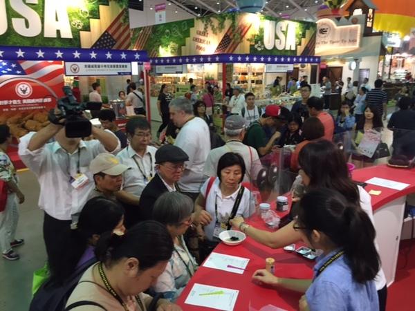 スタッフが集まるお客さんに黒豆を紹介し横でアンケートを書いている女性の様子をテレビカメラが撮影をしている写真