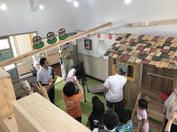10名ほどの大人と子供たちの頭上に細長い透明の筒が通っていて、その筒を大人の人達がスマホで撮影している写真