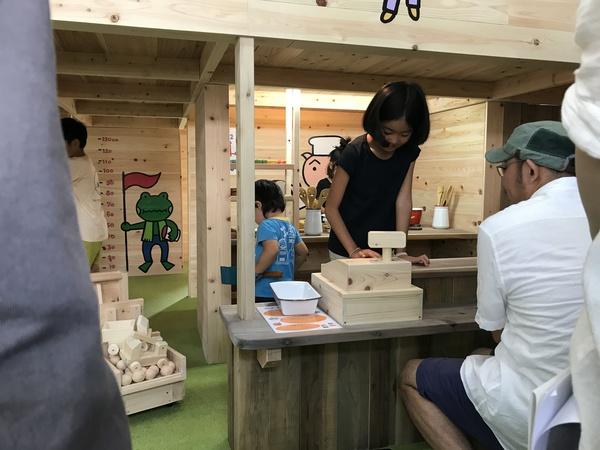 手前に男性が座っていて、その前のテーブルの上にある木で作られたレジで女の子が遊んでいる写真