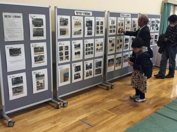 掲示板に「写真でみる140年のあゆみ」が紹介されて、その掲示板を子供や大人が見ている写真