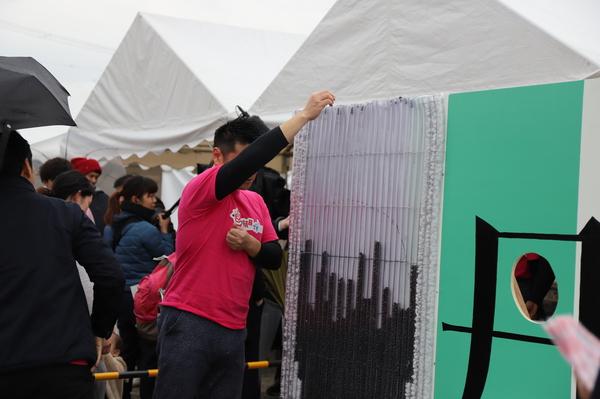 赤いTシャツを着た男性が黒い小さい玉のような物を筒状の枠に入れている写真