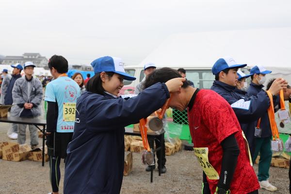 帽子を被った女性が赤のTシャツを着たランナーにメダルをかけている写真