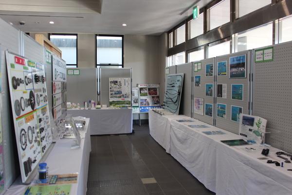 企業が制作している部品がパネルに貼られわかりやすく展示されており、沢山の写真を使って、企業の取り組みを紹介している様子の写真