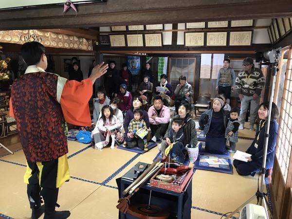 お寺の部屋の前方に立っている方の話を真剣に聞いている方々の写真