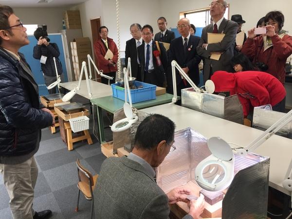 机に設置されたいくつかの拡大鏡の周りに集まり、話を聞く市長と関係者の写真