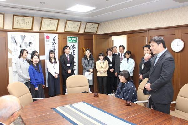 市役所を訪問した田中 美央さんが立って話しているのを座って見ている市長や母親と立って見ている職員らの写真