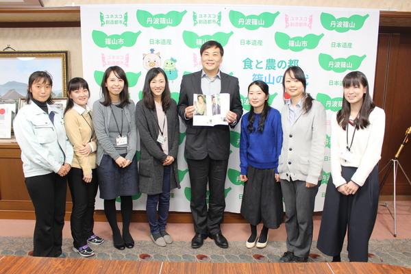 冊子を広げている田中 美央さんを真ん中に女性職員らが並んで記念撮影している写真