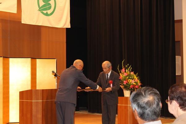 市長が男性に賞状を手渡している様子を会場の後方から写した写真