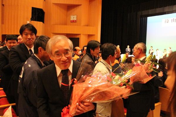 花束を抱え退場する男性退職者の写真