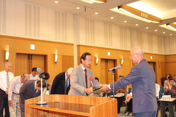 市長が男性に賞状を渡し、賞状をを受け取る男性の後ろで5人の人が礼をしている写真