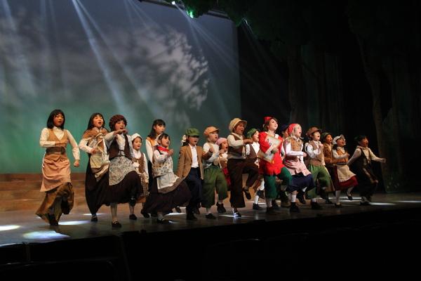 ピノッキオの衣装で左足をそろってあげてダンスをしている多くの出演者の写真