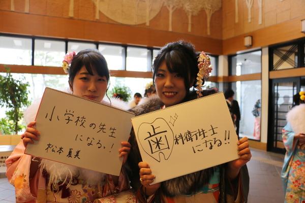 「小学校の先生になる!」「歯科衛生士になる!!」と書いた画用紙を持って写っている、振袖を着た新成人2名の写真