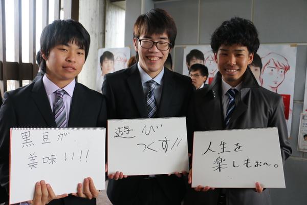「黒豆が美味しい!!」「遊びつくす!!」「人生を楽しもお~」と書いた画用紙を持って写っている、スーツを着た新成人3名の写真
